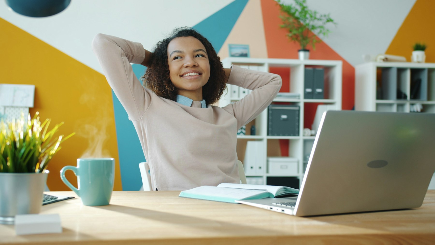 A woman leaning back and smiling at her desk beside a laptop