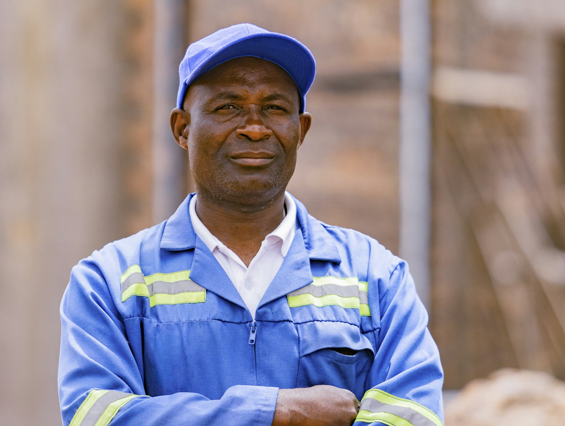 A site worker in blue overalls smiling with his arms folded